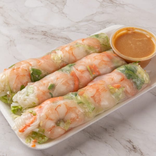 Three fresh spring rolls with shrimp and vegetables, served with a side of peanut sauce.