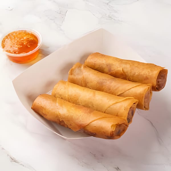 Four crispy golden-brown egg rolls in a white paper tray with a side of sweet chili sauce.