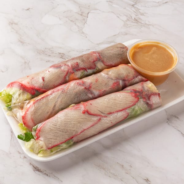 Three fresh spring rolls with red pork and lettuce, served with a side of peanut sauce.