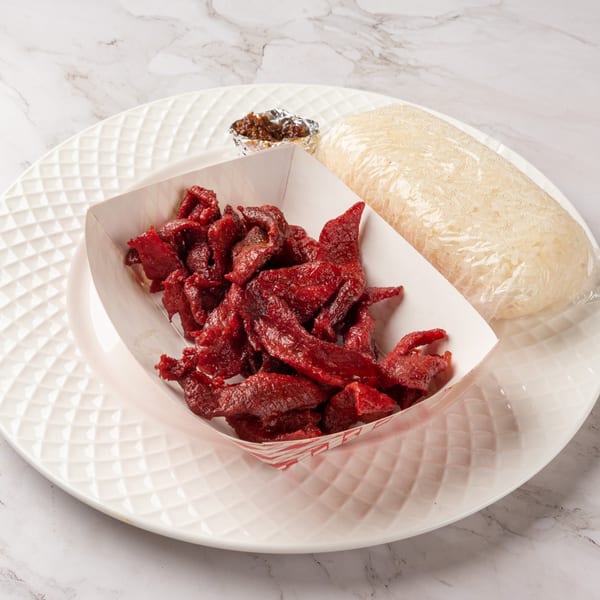 Laos beef jerky in a paper tray, sticky rice, and chili sauce on a white plate.
