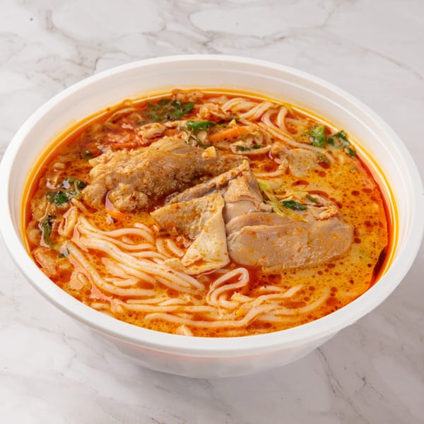 Close-up of a bowl of spicy Lao curry noodle soup with chicken and herbs.