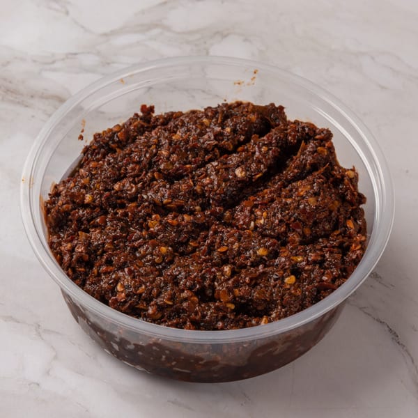 A clear plastic container filled with a dark, chunky, spicy Lao chili paste.
